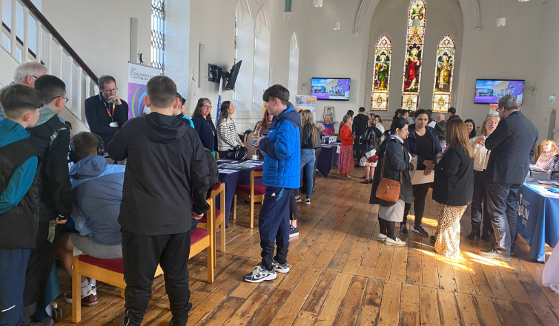 Groups of students and mature students standing chatting in group attending education fair in church