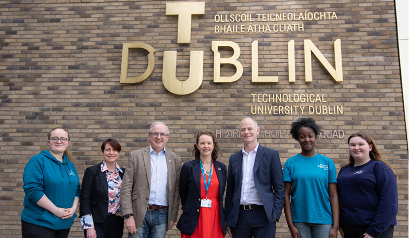 Woman, and two men posed with the climate stripes graphic in front of the TU Dublin sign