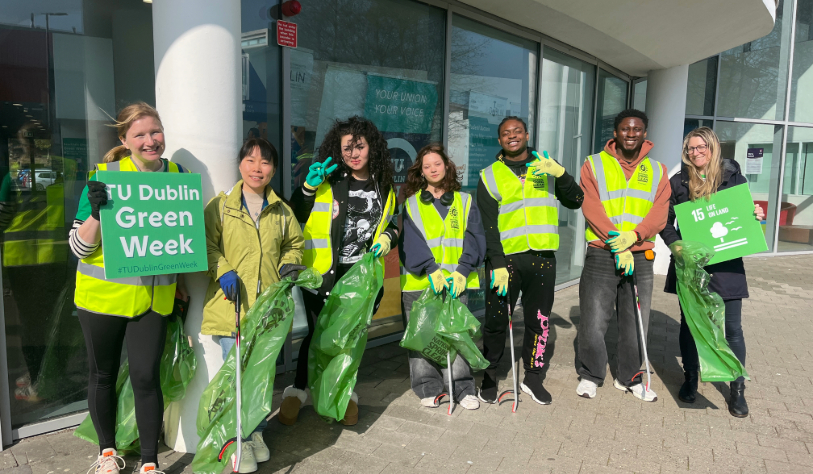 7 people pose for photo holding rubbish bags and litter pickers. Two hold signs, one for sdg life on land, the other TU Dublin Green Week