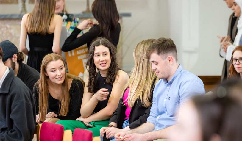 students sitting in a row at an event, smiling and chatting