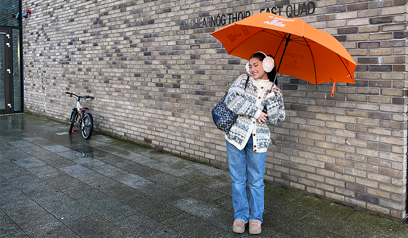 photo of girl holding orange SDG 11 Umbrella in front of brick wall