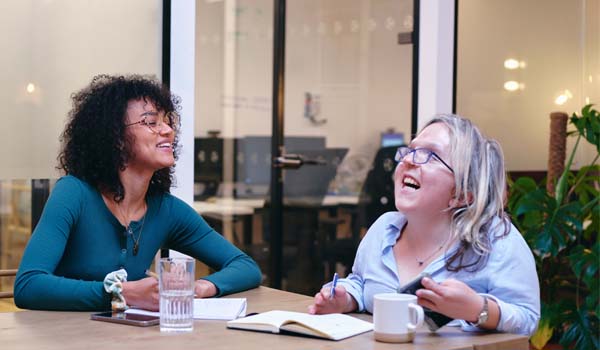 Two smiling women writing in notebooks in modern office