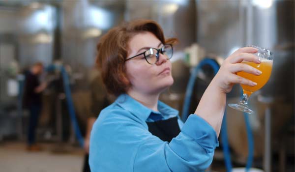 Portrait of woman brewer holding glass with craft beer and drinking