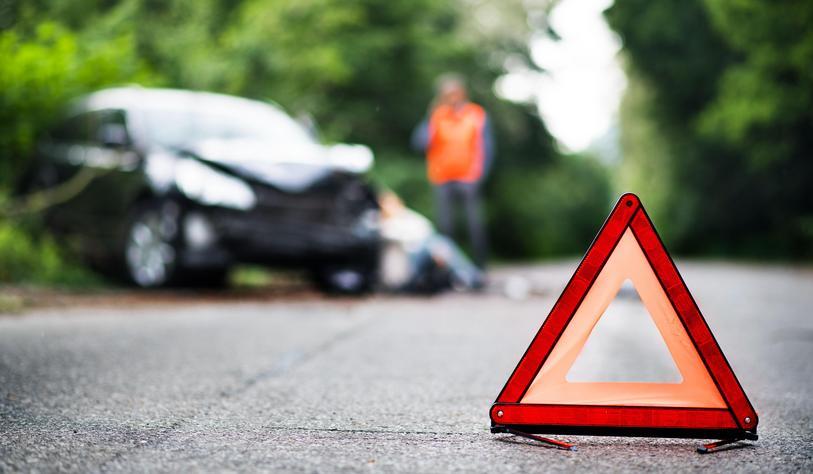 A close up of a red emergency triangle on the road in front of a car after an accident.