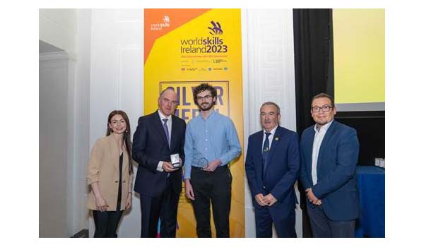 A group of people standing in front of a Worldskills pull banner with one person receiving an award