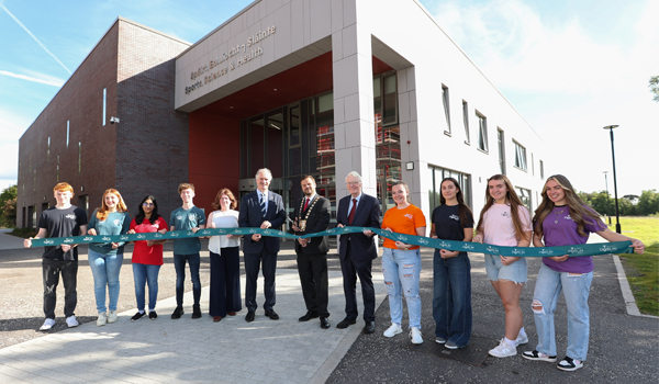 A group of people holding a ribbon outside the a large building