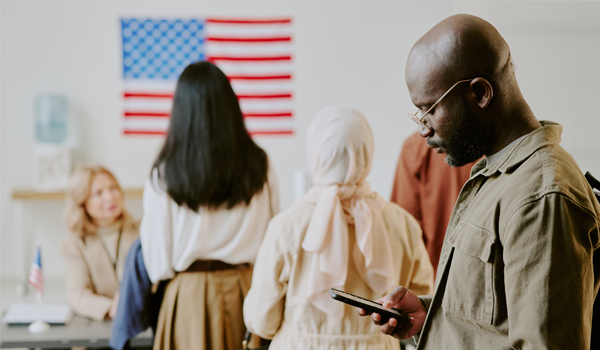 A group of people queue to vote with a US flag in front of them